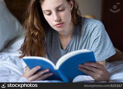 Young woman reading book on bed. concepts of home and comfort.
