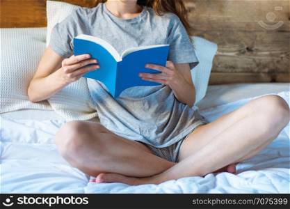 Young woman reading book on bed. concepts of home and comfort.