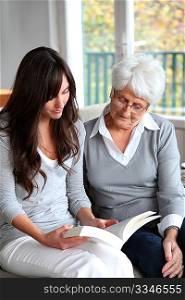 Young woman reading book to elderly woman