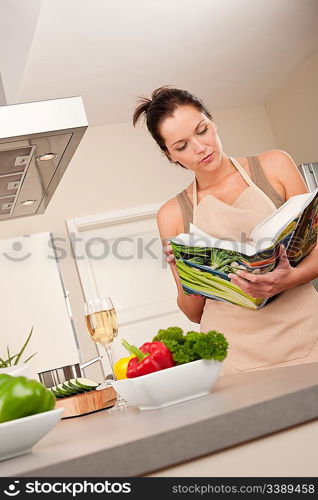 Young woman reading cookbook in the kitchen, looking for recipe