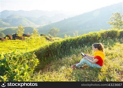 Young woman reading digital tablet at tea plantations near Munnar, Kerala, India