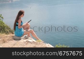 young woman reading e-book while sitting by the sea