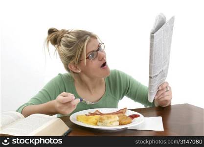 Young woman reading newspaper at breakfast. Shocked expression on face. Shot in studio over white.