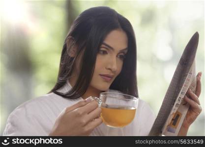Young woman reading newspaper while drinking tea