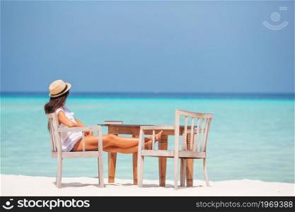 Young woman reading on tropical white beach in outdoor cafe. Young woman reading at outdoor beach cafe