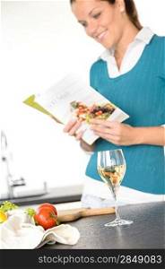 Young woman reading recipe cooking book preparing salad wine kitchen