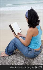 Young woman reading sitting on a stone of the beach