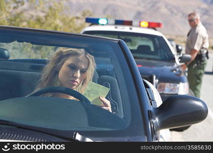 Young woman reading speeding ticket, policeman in background