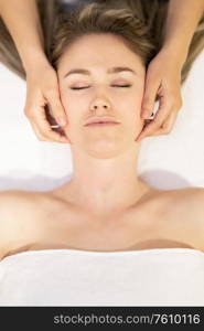 Young woman receiving a head massage in a spa center. Female patient is receiving treatment by professional therapist.. Young blond woman receiving a head massage in a spa center.