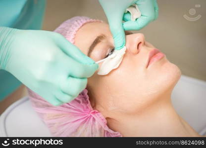 Young woman receiving eyelash removal procedure and removes mascara with a cotton swab and stick in a beauty salon. Young woman receiving eyelash removal procedure and removes mascara with a cotton swab and stick in a beauty salon.