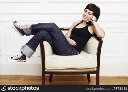 Young woman reclining in an armchair and talking on a mobile phone