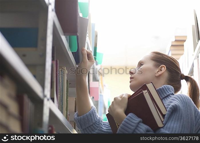 Young woman references library books on shelves