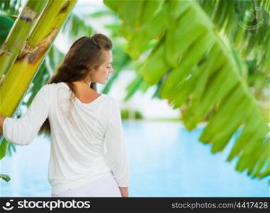 Young woman relaxing among tropical palms. Rear view