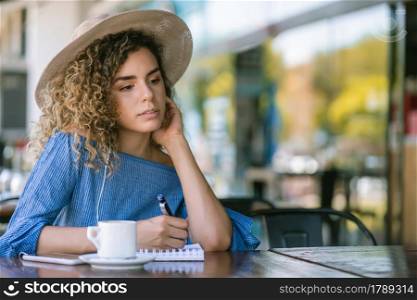 Young woman relaxing and writing on a notebook while drinking a cup of coffee at a coffee shop.
