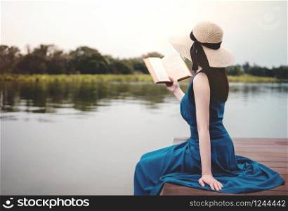 Young Woman Relaxing by Riverside. Sitting on Deck and Reading Book. Unplugged Life Concept