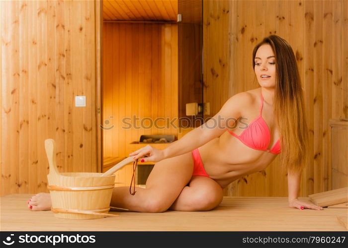 Young woman relaxing in sauna. Spa wellbeing.. Young woman with bucket and ladle relaxing in wood finnish sauna. Attractive girl in bikini resting. Spa wellbeing pleasure.