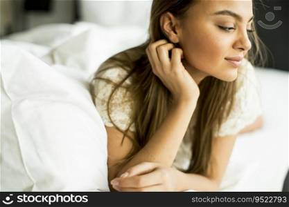 Young woman relaxing in white bed after waking up