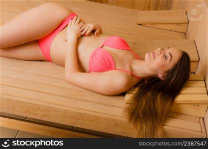 Young woman relaxing in wooden finnish sauna. Attractive girl in bikini resting. Spa wellbeing pleasure. Healthy lifestyle.. Young woman relaxing in sauna. Spa wellbeing.