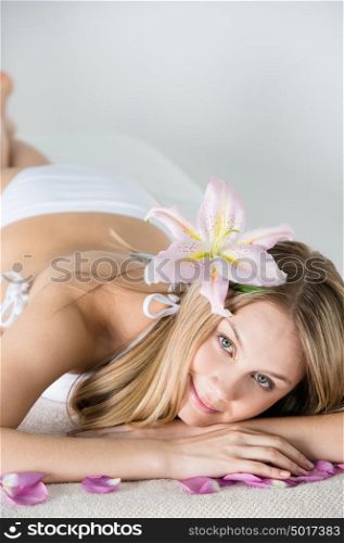 Young woman relaxing on massage table in health spa with flower in her hair and petals around her