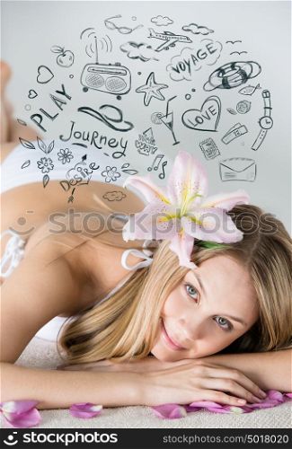 Young woman relaxing on massage table in health spa with flower in her hair and petals around her. Her dreams are sketched overhead