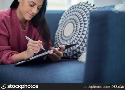 Young Woman Relaxing On Sofa At Home Writing In Journal