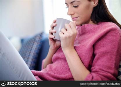 Young Woman Relaxing On Sofa With Hot Drink