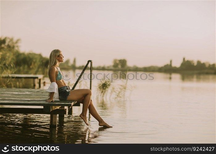 Young woman relaxing on the pier by the lake at summer day