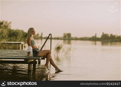 Young woman relaxing on the pier by the lake at summer day