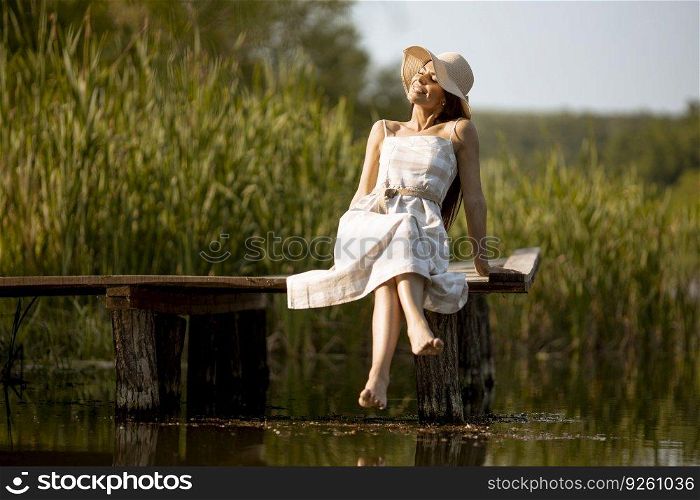 Young woman relaxing on the woodenπer at the calm lake on a hot∑mer day