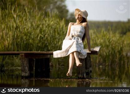Young woman relaxing on the woodenπer at the calm lake on a hot∑mer day