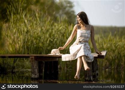 Young woman relaxing on the wooden pier at the calm lake on a hot summer day