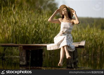 Young woman relaxing on the wooden pier at the calm lake on a hot summer day