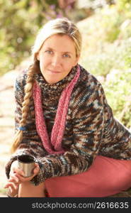 Young Woman Relaxing With Thermos Flask In Autumn Landscape