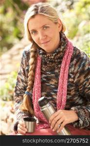 Young Woman Relaxing With Thermos Flask In Autumn Landscape