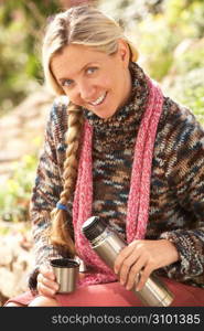 Young Woman Relaxing With Thermos Flask In Autumn Landscape