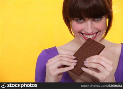 young woman relishing chocolate bar against yellow background