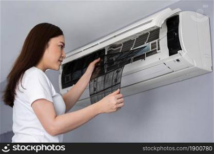 young woman removing air filter of the air conditioner for cleaning at home