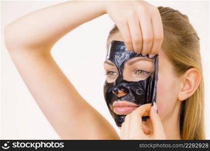 Young woman removing carbo black peel-off mask from her face, on white. Teen girl taking care of oily skin, cleaning the pores. Beauty treatment. Skincare.. Girl removes black mask from face