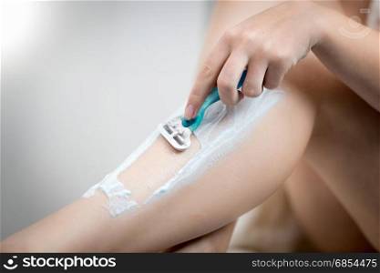 Young woman removing hair on legs with razor at bathroom