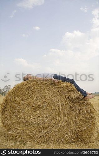 Young woman resting on hay bale in field