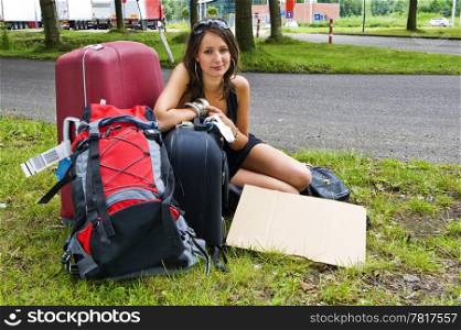 Young woman, resting on her bags, resting at a highway parking lot on her journey