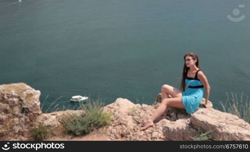 young woman Resting on the cliff near the Black Sea, Bay of Balaclava, Crimea In the background, a pleasure boat sails