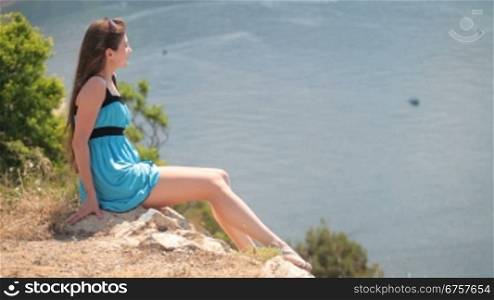 young woman resting on the edge of a cliff by the sea