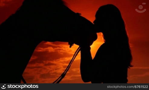 Young woman rider kissing her horse at sunset