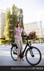 Young woman riding an electric bicycle and using mobile phone in urban environment