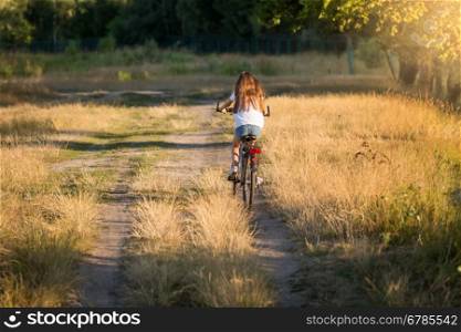 Young woman riding bicycle on dirt road at meadow
