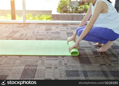 Young woman rolling mat after a yoga on carpet floor, Yoga conce. Young woman rolling mat after a yoga on carpet floor, Yoga concept. Young woman rolling mat after a yoga on carpet floor, Yoga concept