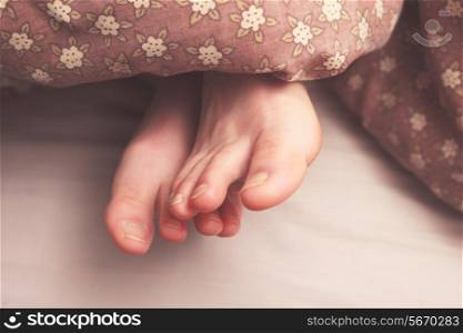 Young woman&rsquo;s feet in bed under the covers