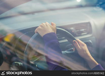 Young woman's hand holding on black steering wheel while driving in the car. view from the outside of the car.. Young woman's hand holding on black steering wheel while driving in the car. view from the outside of the car