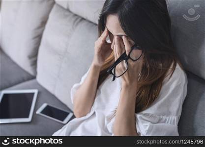Young woman rubbing her eyes feel painful and take off her glasses siiting on sofa and rest one&rsquo;s eyes at home. Young woman take off her glasses and siiting on sofa
